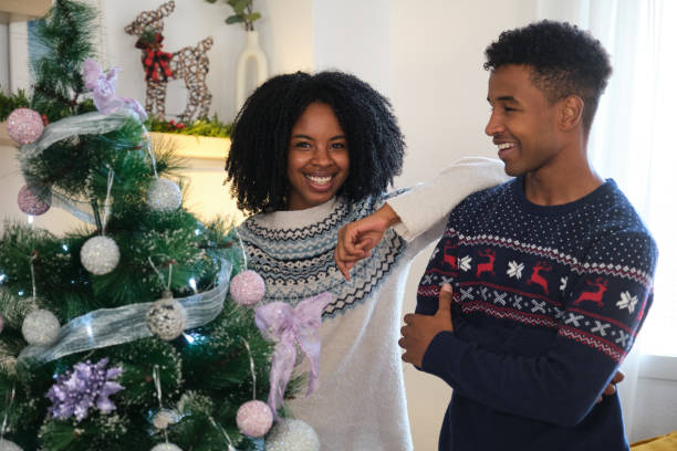 istock Young couple smiling and decorating Christmas tree at home 2180257156