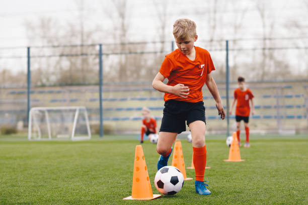 istock Boy Soccer Player In Training. Boy Running Between Cones During Practice in Field on Sunny Day. Young Soccer Players at Speed and Agility Practice Session 2180257990