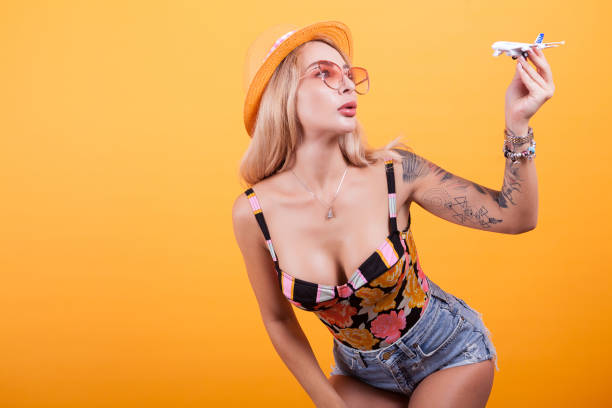 attractive blonde haired woman playinh with plane pver yellow background