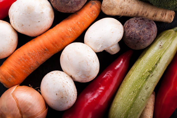 Closeup of fresh, imperfect, organic produce. There is mushrooms, peas, pepper, lettuce, tomato, lemon, and avocado.