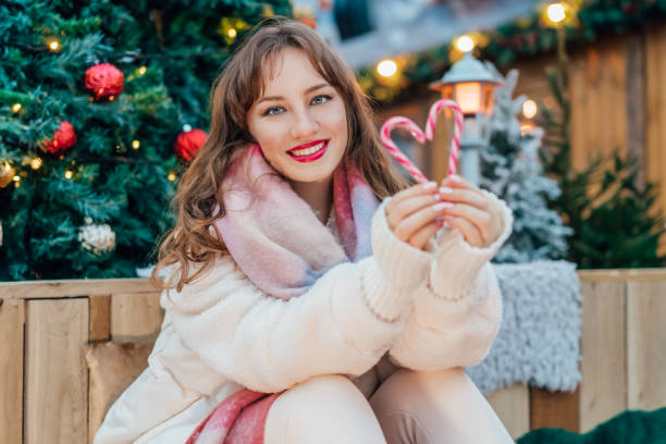 istock Young smiling woman making heart shape with candy canes on a decorated Christmas tree background. Happy New Year celebration Christmas holidays. Time to share love, and charity concept. Vertical card 2180271612