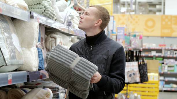 istock Man carefully selecting a soft blanket in a cozy store, weighing his options. Perfect for adding warmth and comfort to any bedroom or living room 2180278045
