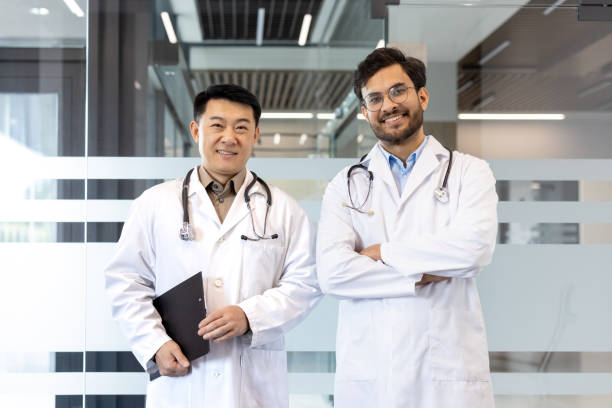 Two confident doctors standing together in modern medical facility while smiling at camera, conveying professionalism and teamwork. Ideal for healthcare, teamwork, and professional collaboration themes.
