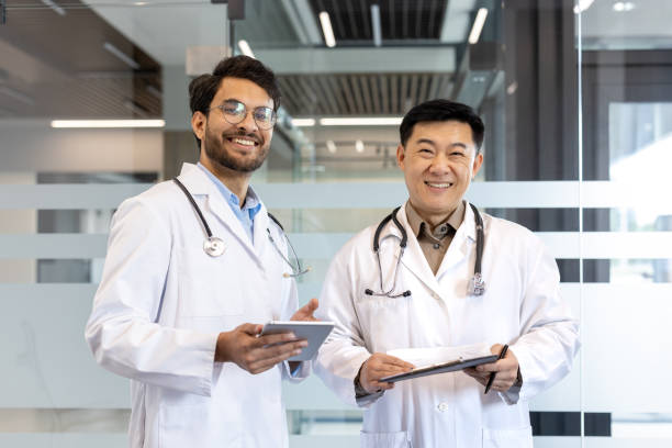 istock Two smiling doctors in white coats with stethoscopes standing in modern medical office holding digital tablet and clipboard, promoting teamwork and professional healthcare environment 2180284054