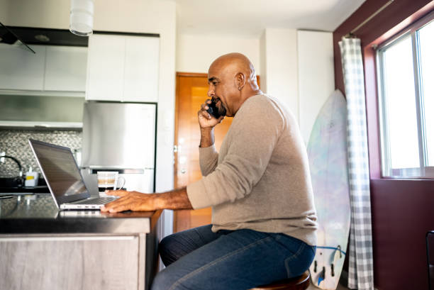istock Senior man talking on mobile phone and using laptop at home 2180287417
