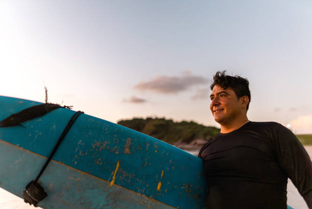 istock Mid adult surfer man contemplating while looking away on the beach 2180288108