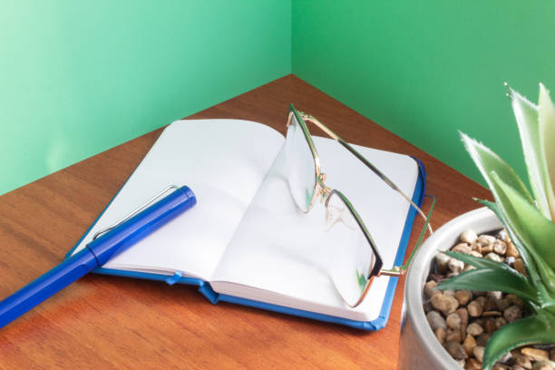 An elegant pen and glasses on an open blank notebook surrounded by green walls. Workspace. Handwriting.