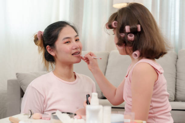istock Young girl playfully applying lipstick on mothers lips during an intimate makeup session. mother smiles warmly, enjoying the affectionate and joyful moment with her daughter in living room setting. 2180290265