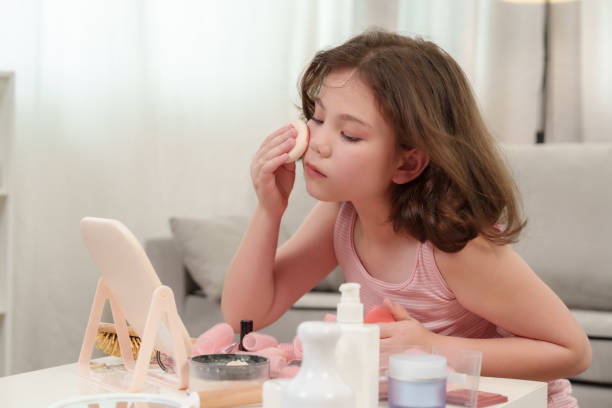 istock Young girl gently applying makeup with a sponge while practicing in front of a small mirror. The scene captures the innocence and concentration of a child learning and enjoying the moment. 2180290288