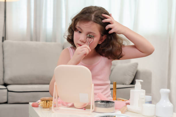 istock Young girl using an eyelash curler while sitting in front of mirror, practicing makeup techniques. concentration and delicate handling of curler joy and creativity of a child learning self-expression. 2180290296