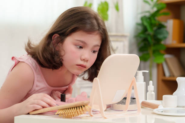 istock Young girl looking closely at her reflection in the mirror while practicing her makeup skills. Her curiosity and focus show the innocence of a child exploring self-expression and beauty. 2180290300