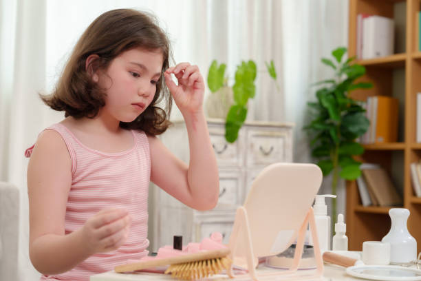 Young girl adjusting her hair in front of a mirror while practicing makeup techniques. The scene captures the calm and focused joy of a child learning to style and enhance her appearance.