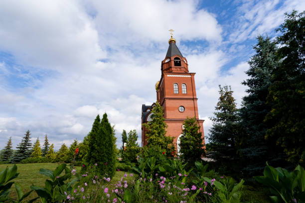 istock A large and impressive red brick building, featuring a prominent clock tower, is encircled by lush, green trees and vibrant flowers, creating a picturesque scene for all to enjoy 2180291338