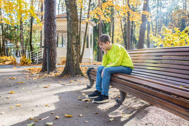sad boy sitting on a bench in an autumn park on a sunny day