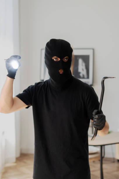 istock Masked burglar holding crowbar and flashlight searching for valuables 2180294076
