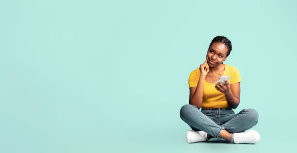 istock Thoughtful African American Lady Sitting Using Cellphone, Blue Background 2180300231