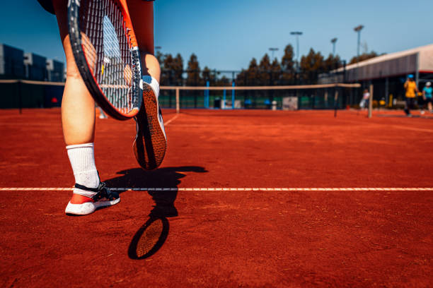 istock Female tennis player cleans clay from sneakers with racket 2180304707