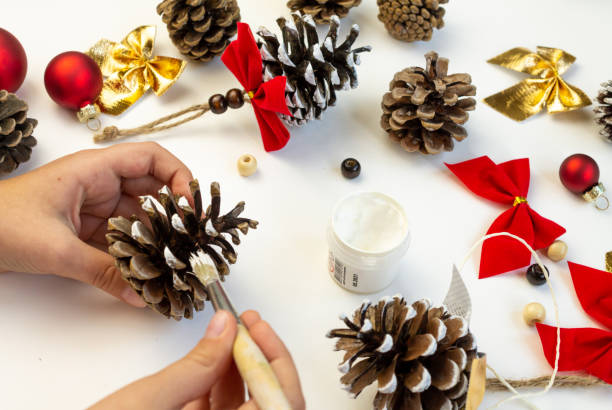 istock Toy for the Christmas tree from pine cones. Children's creativity. Hands close-up paint the cone with white paint. 2180304710