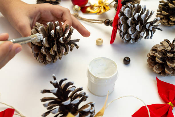 istock Toy for the Christmas tree from pine cones. Children's creativity. Hands close-up paint the cone with white paint. 2180304923