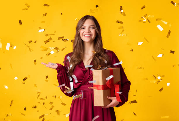 istock Happy lady holding present standing under confetti shower over colorful background 2180309731