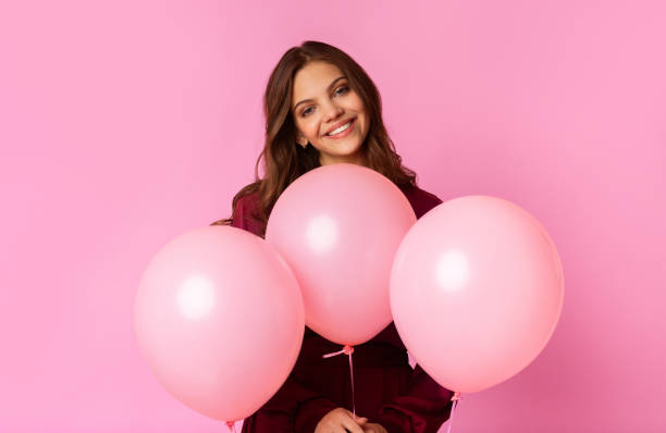istock Positive lady posing with three rosy balloons, standing over colorful background 2180309767
