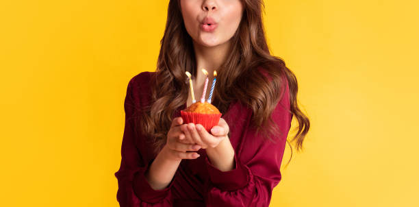 istock Unrecognizable woman blowing colourful candles on birthday cupcake 2180309809