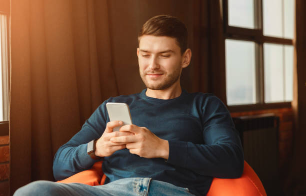 istock Student Using Phone Texting Sitting In Beanbag Chair Indoor 2180316143