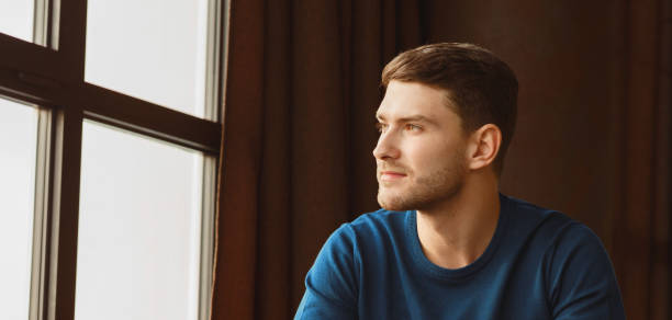 istock Young Man Looking Aside Sitting Near Window Indoor 2180316152