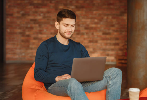 istock Man With Laptop Sitting In Beanbag Chair Working In Workspace 2180316311