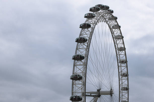 London, UK - October 14, 2022 - Black and white image showcasing the iconic London Eye and a historic building architecture against cloudy and moody sky in the background.