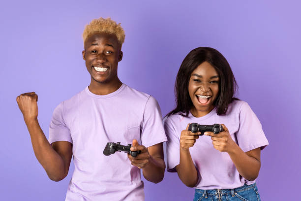 istock Fun hobbies. Cool black guy playing video games with his girlfriend on lilac background. Panorama 2180322737