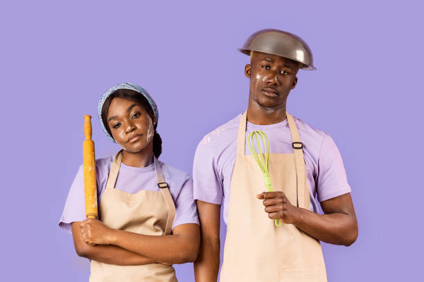 istock Exhausted black couple with kitchen utensils having hard time baking on color background 2180322758