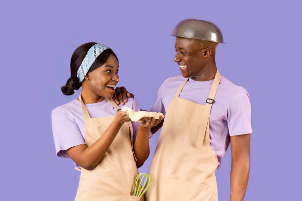istock Cheerful black girlfriend and boyfriend enjoying their baking activity on lilac background 2180322793