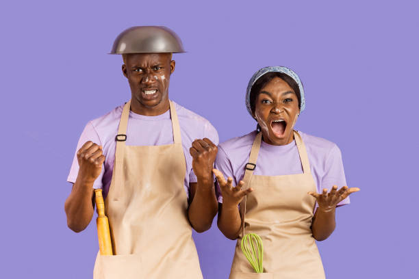 istock Millennial black lady and her boyfriend shouting from anger while attempting to bake on lilac background 2180322813