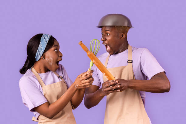 istock Emotional African American lady and guy fighting with kitchen utensils while cooking on color background 2180322814