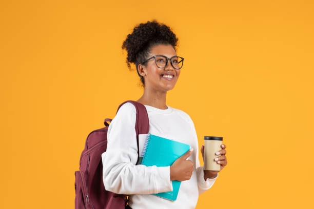 Cheerful student holding a coffee cup and notebook against a bright backdrop