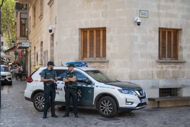 28.09.2024 Sóller, Spain. Two members of the Guardia Civil stand by their patrol car in Mallorca, casually chatting while on duty in a quiet, cobblestone street corner, reflecting the local atmosphere of safety and community presence.
