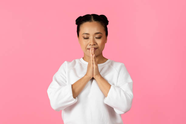 Woman practicing mindfulness with hands together in front of a pink backdrop
