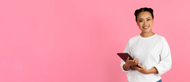 istock A young woman smiling while holding a tablet in front of a pink background 2180326321