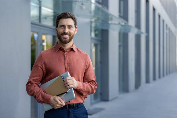 istock Confident businessman standing outside modern office building holding digital tablet and notebook 2180326697