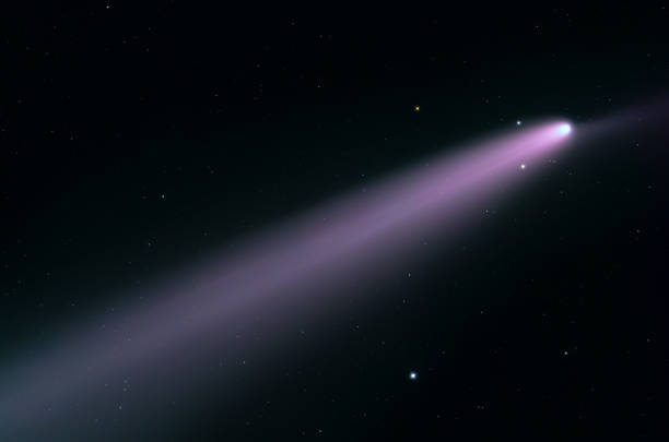 The comet traveling through space, with a long, bright tail extending outward. The tail is colored in a striking purple or pinkish hue.