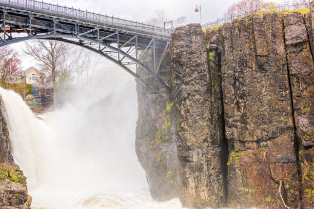 istock Paterson Great Falls in spring with mist rising from powerful water cascading over cliffs under cloudy sky. New Jersey. USA. 2180330120