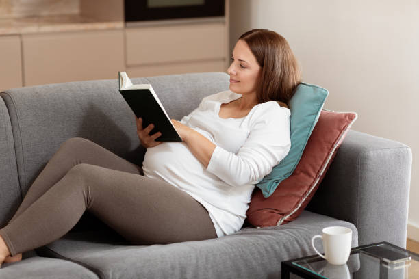 Pregnant woman relaxing on a sofa while reading a book at home