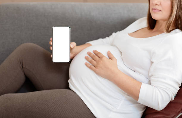 istock Expecting mother relaxing on a couch while holding a smartphone at home 2180334522