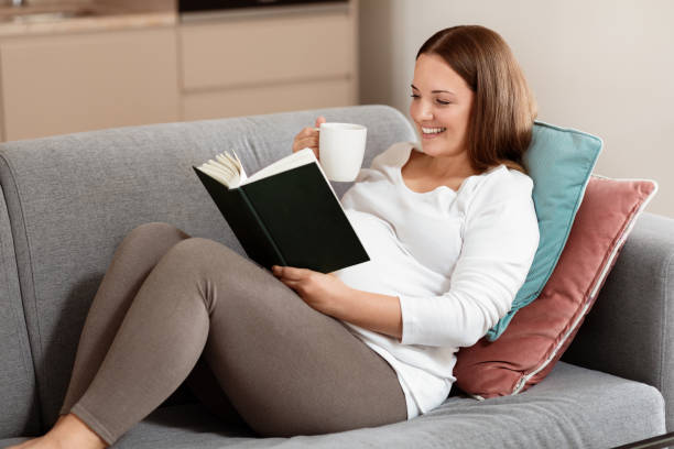 istock Woman enjoying a book while relaxing on a sofa with a cup of tea 2180334533