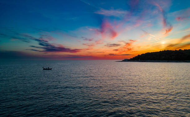 Clouds reflect on the calm waters under the fading light of sunset, creating a mesmerizing seascape.