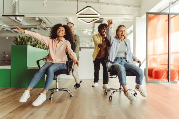 istock Cheerful businesspeople having fun racing on office chairs at workplace 2180342522