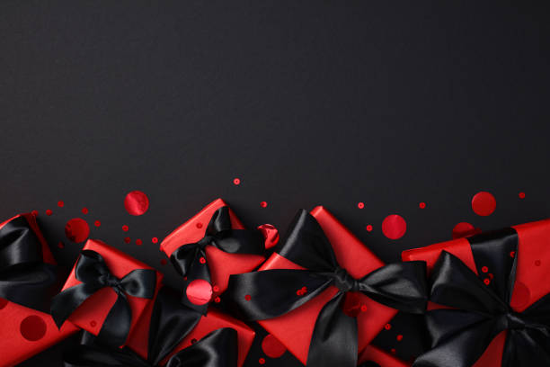 istock Black Friday sale poster design. Black gift boxes with a satin bow, surrounded by vibrant red confetti 2180342943