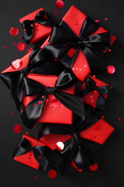 istock Elegant red gift boxes with satin black ribbons, set against a dark background. Black Friday sale presents 2180342982