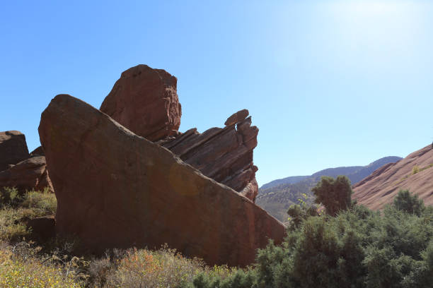 A striking rock formation stands resilient against a bright blue sky, surrounded by lush greenery and vibrant vegetation, showcasing natures beauty and geological wonders.